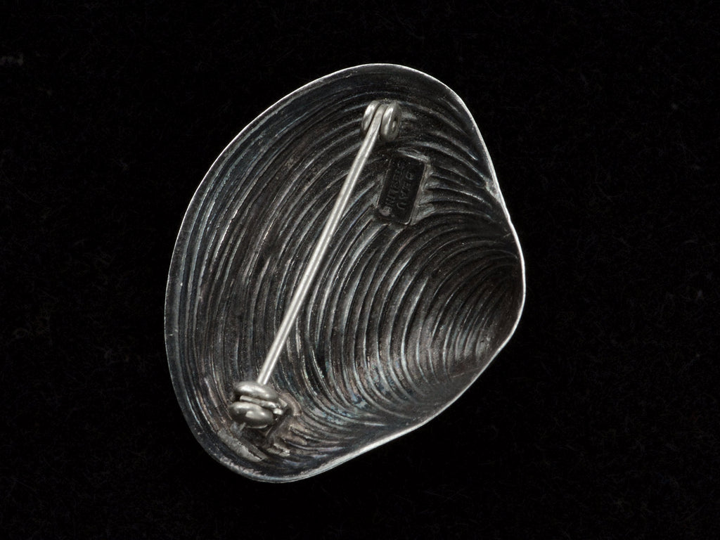Reverse view of silver ribbed clam shell brooch showing pin fittings and a maker's mark that reads "BEAU STERLING". On black background.