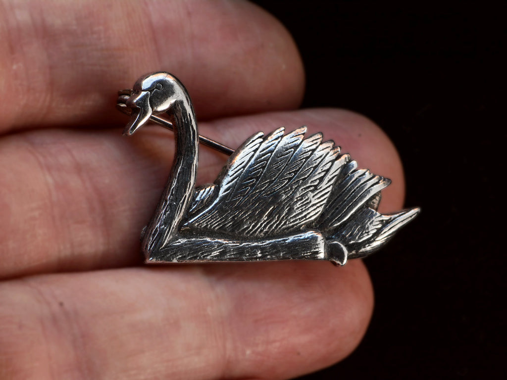 A sterling silver swan brooch on held in hand.