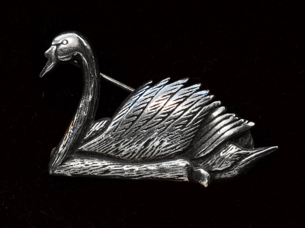 A sterling silver swan brooch on black background.