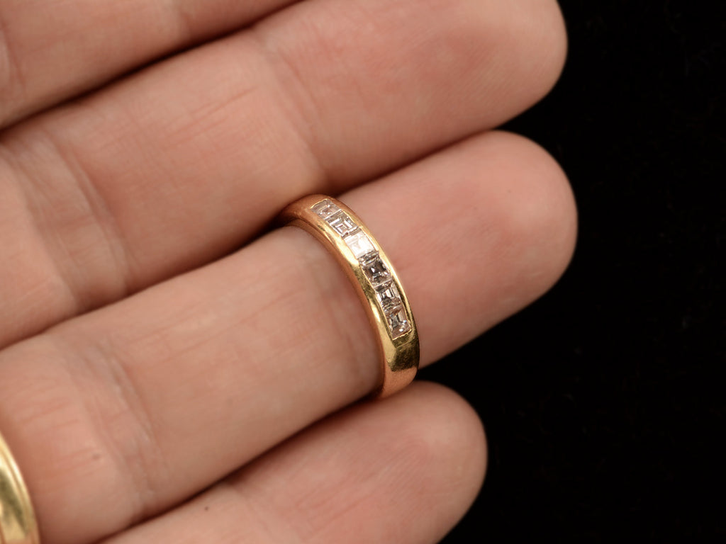 A vintage yellow gold band channel-set with six rectangular step cut diamonds, shown on finger