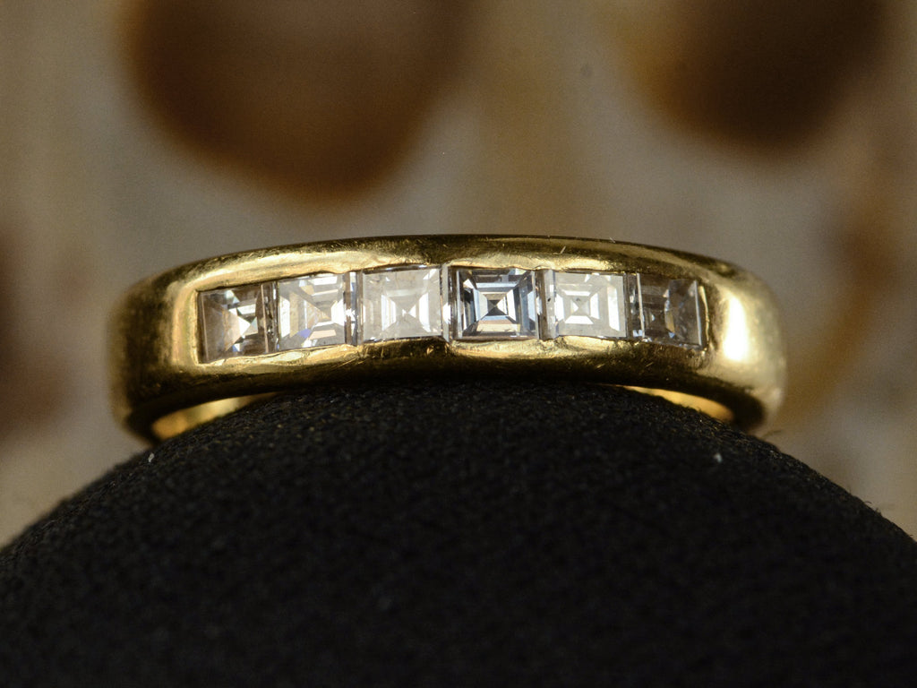 Close up of a a vintage yellow gold band channel-set with six rectangular step cut diamonds, shown on dark background