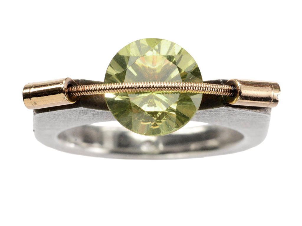 Plodowski ring with a green stone tension set with yellow gold against a silver mounting, shown on white background.