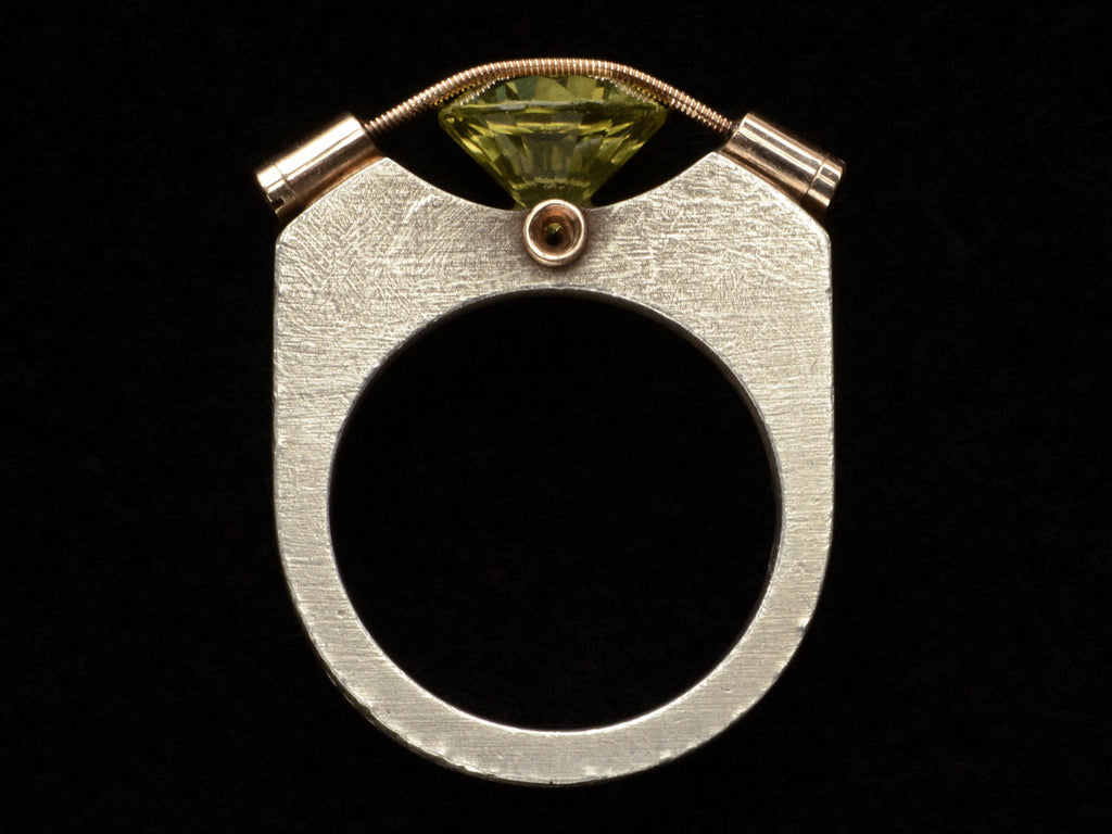 Side profile of Plodowski ring with a green stone tension set with yellow gold against a silver mounting, shown on black