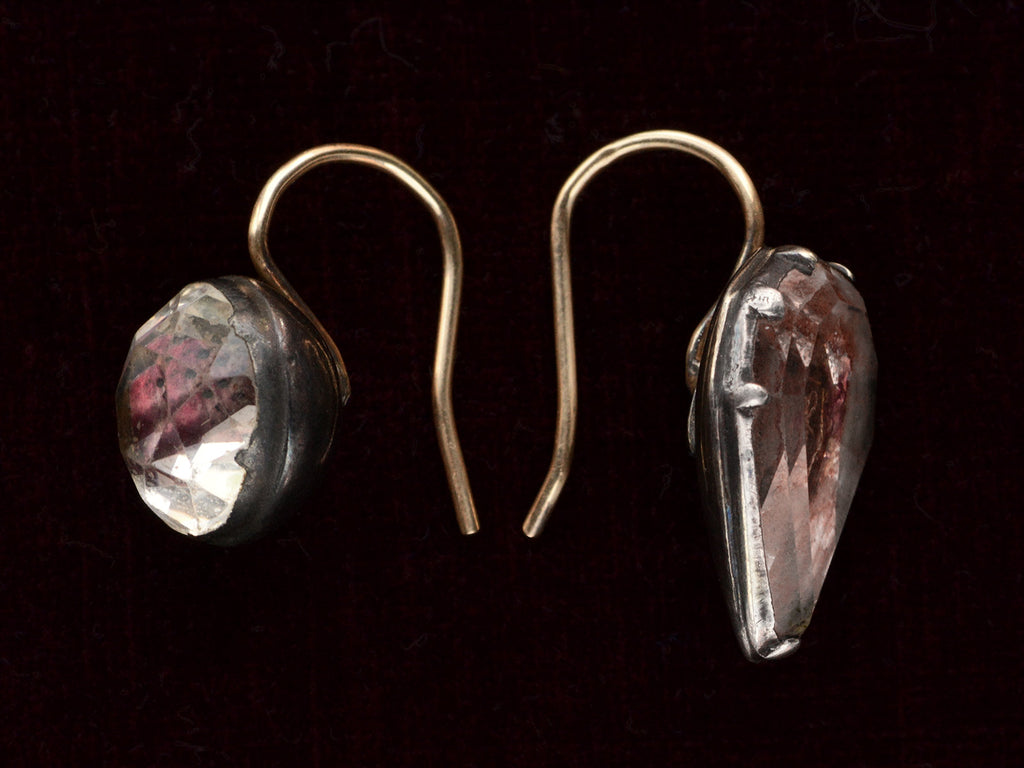 Side view of mismatched earrings made from pink foiled silver set buttons on gold ear wires. On black background.