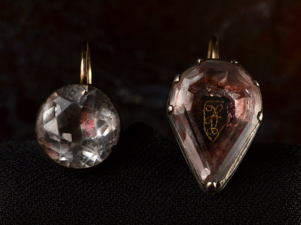Front view of mismatched earrings made from pink foiled silver set buttons on gold ear wires. On black background.