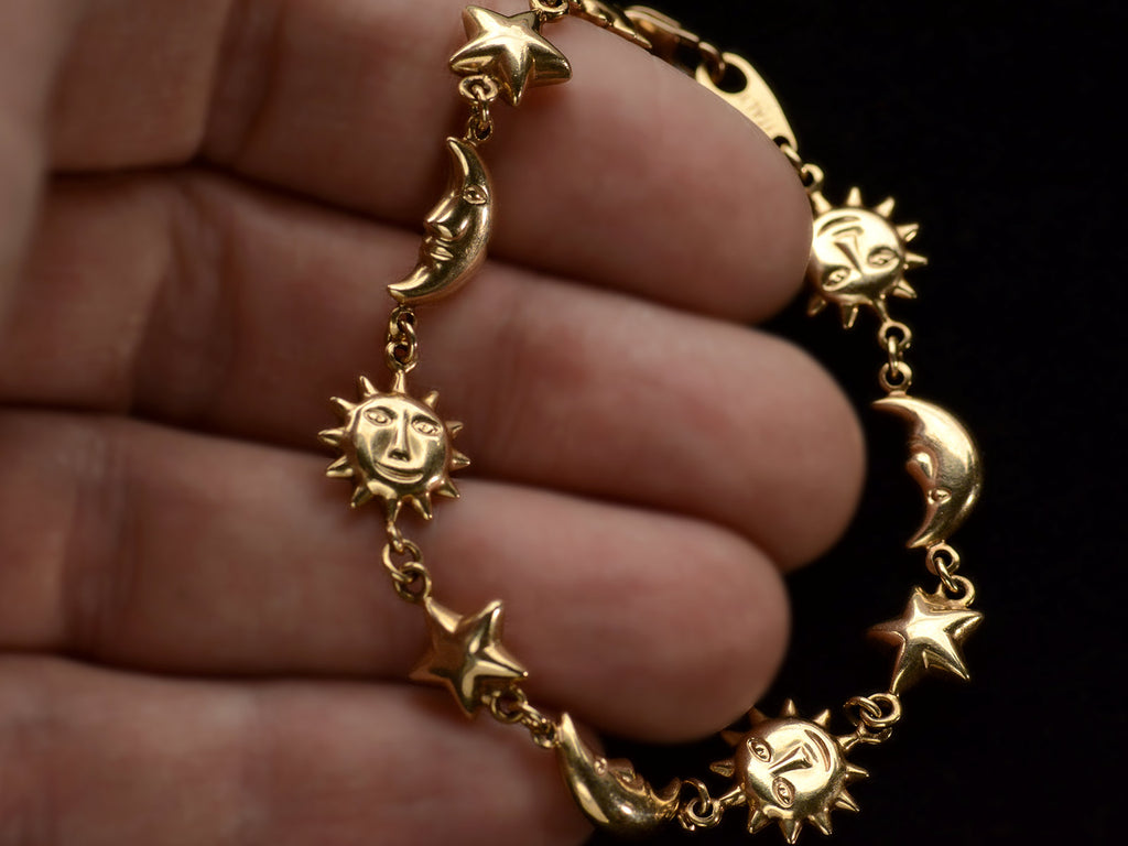 A yellow gold bracelet with figural links depicting suns, stars and moons, on hand.