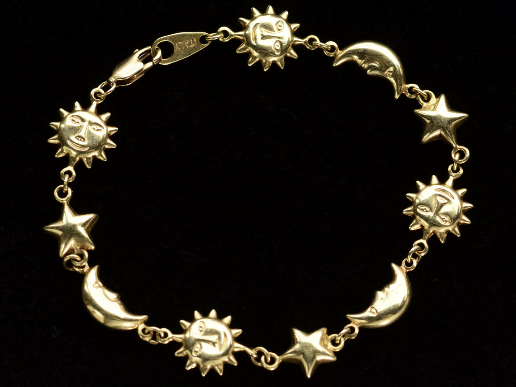 A yellow gold bracelet with figural links depicting suns, stars and moons, on dark background.