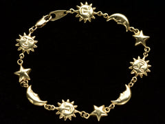thumbnail of A yellow gold bracelet with figural links depicting suns, stars and moons, on dark background.