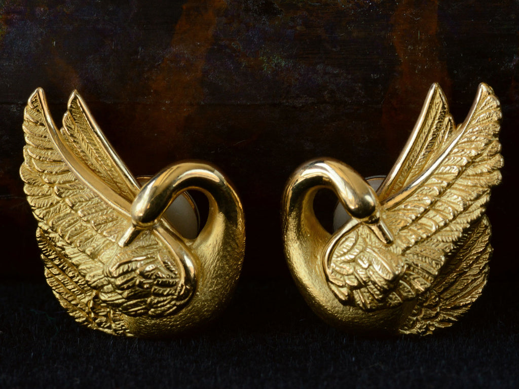 Pair of vintage swan-shaped 18K yellow gold earrings on dark background.