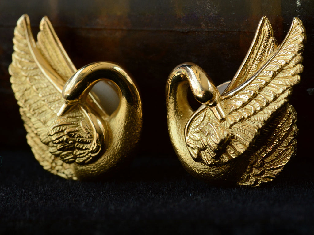 Angled front view of pair of vintage 18K yellow gold swan earrings, on dark background.