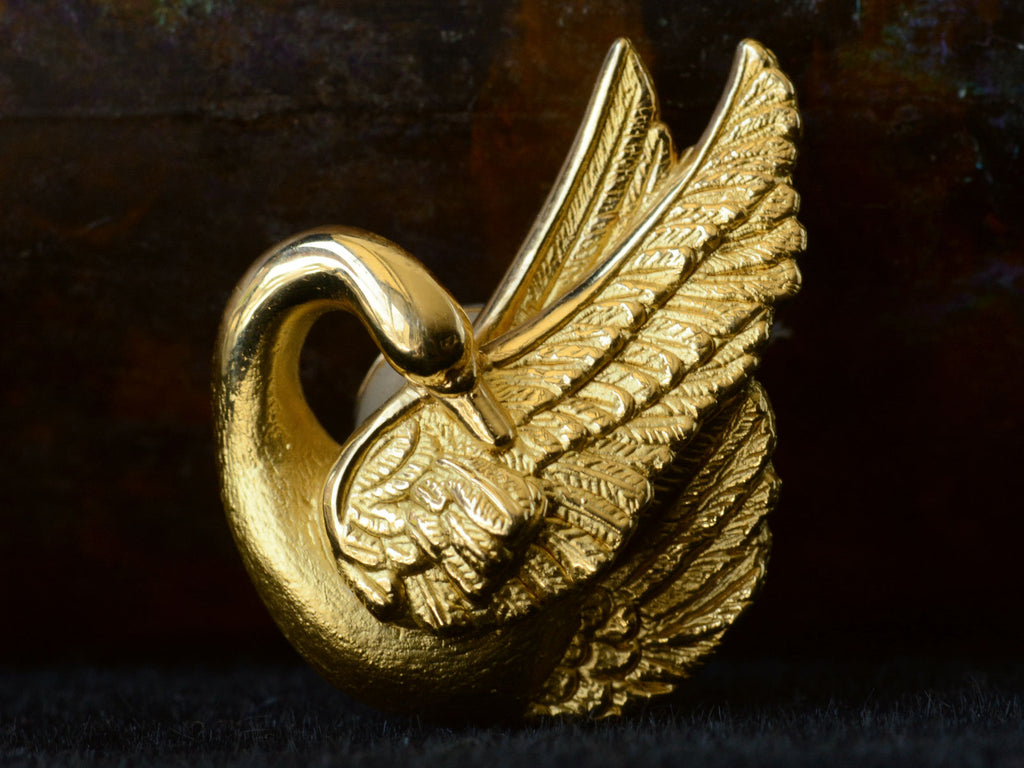 Detail of single 18K yellow gold swan earring on dark background.