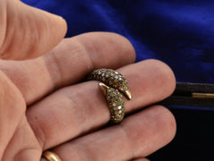 thumbnail of Figural ring with two swan heads, set with light yellow diamonds and ruby eyes in silver, shown on finger.