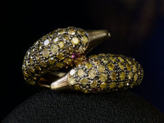 thumbnail of Front view of a figural ring with two swan heads, set with light yellow diamonds and ruby eyes in silver, shown on dark background.