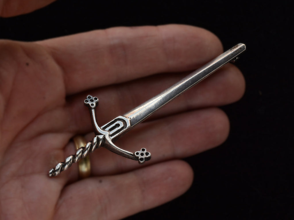 Large silver sword brooch held in hand.
