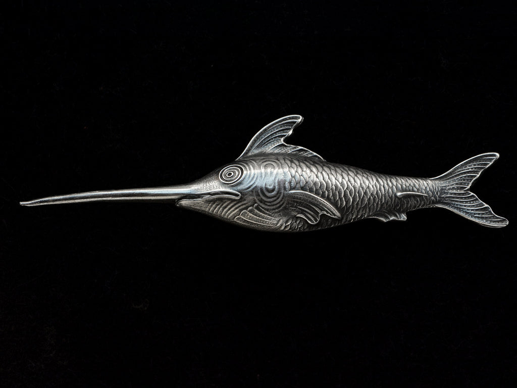 Antique silver sewing stiletto in the form of a swordfish, shown on black background.