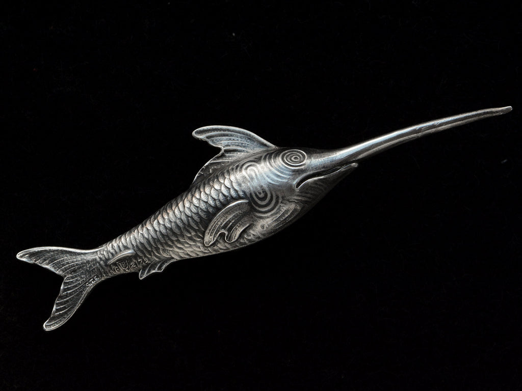 Backside of antique silver sewing stiletto in the form of a swordfish, shown on black background. Stamps visible reading "STERLING" and "2179"