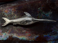 thumbnail of Backside of antique silver sewing stiletto in the form of a swordfish, shown on dark iridescent background. Stamps visible reading "STERLING" and "2179"