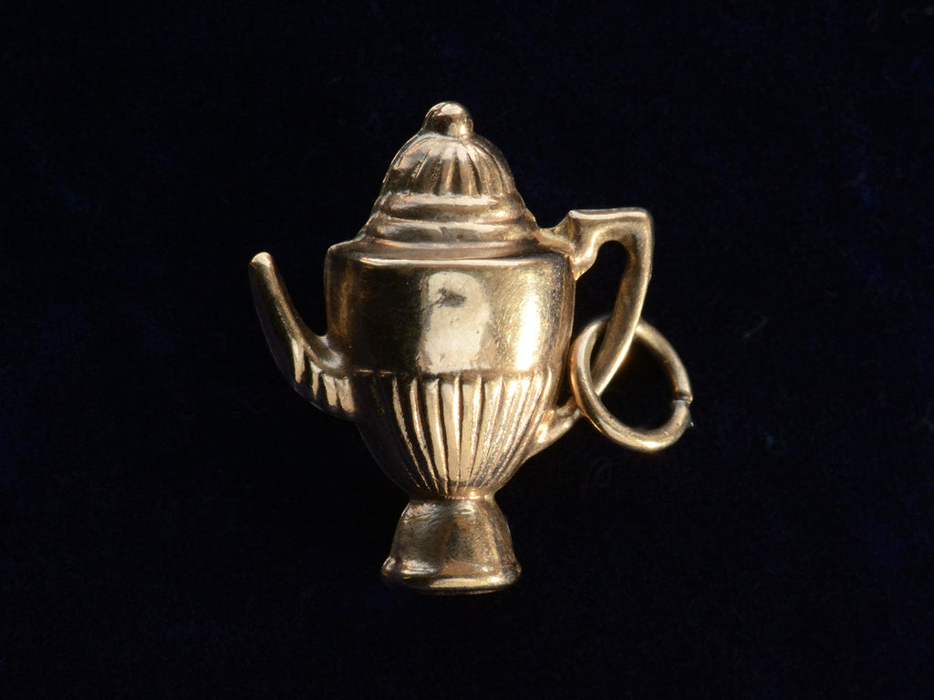 A gold 1964 Gold Teapot Charm shown on black background