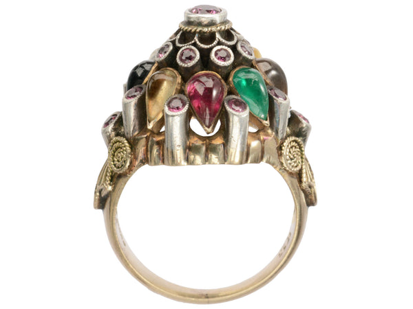 Side profile of tall tiered vintage ring set with rubies, and colorful gemstones in silver and gold. On white background.