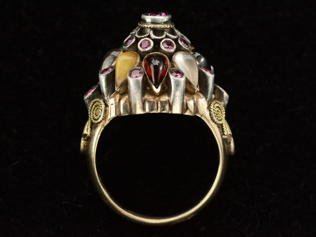 Alternate side profile of tall tiered vintage ring set with rubies, and colorful gemstones in silver and gold. On black background.