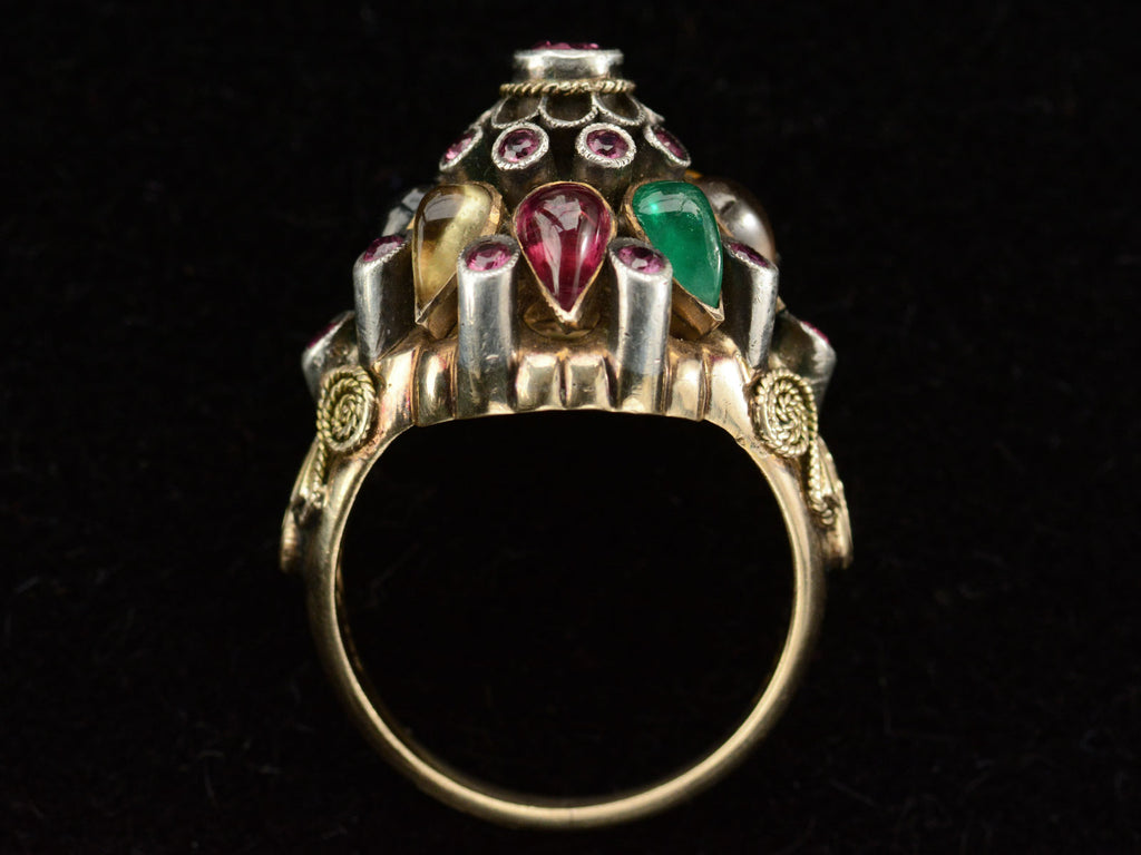 Side profile of tall tiered vintage ring set with rubies, and colorful gemstones in silver and gold. On black background.