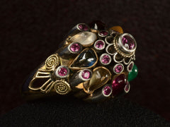 thumbnail of Opposite angled view of tall tiered vintage ring set with rubies, and colorful gemstones in silver and gold. On dark background.
