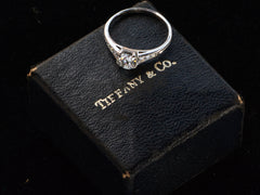thumbnail of Elevated view of a c1930 Art Deco Tiffany & Co platinum engagement ring with a round old cut diamond and three smaller diamonds on each shoulder, shown sitting on top of its original "TIFFANY & CO" stamped ring box