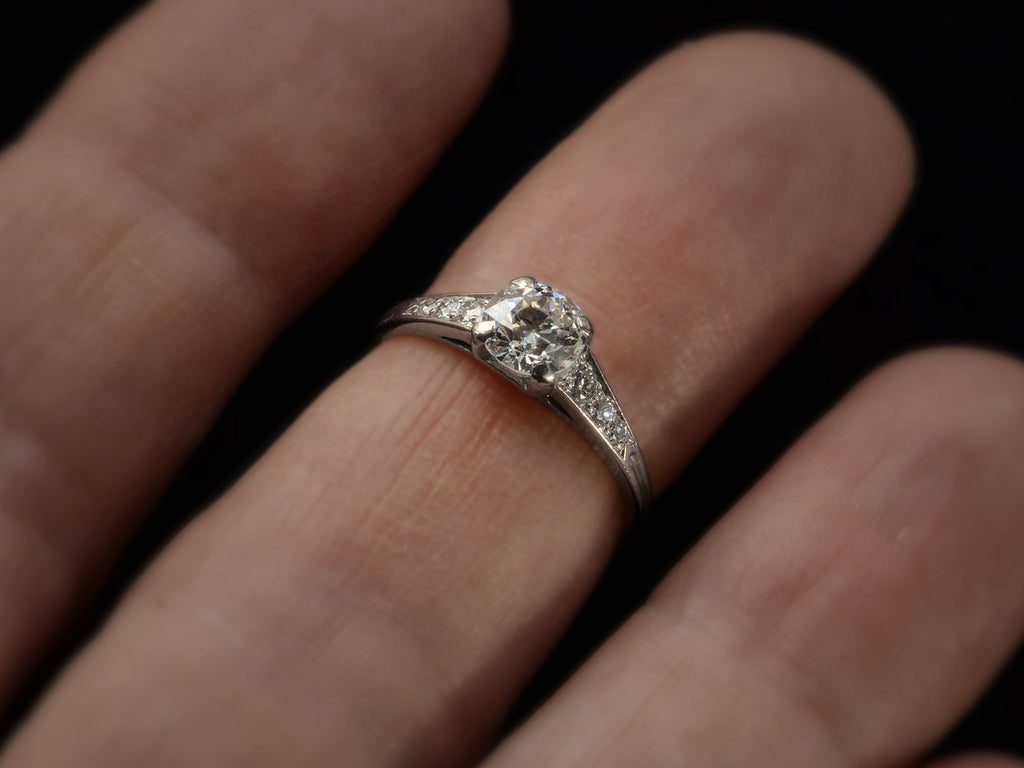A c1930 Art Deco Tiffany & Co platinum engagement ring with a round old cut diamond and three smaller diamonds on each shoulder, tapering in size shown on finger.