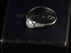 thumbnail of Angled view of a c1930 Art Deco Tiffany & Co platinum engagement ring with a round old cut diamond and three smaller diamonds on each shoulder, shown sitting on top of its original "TIFFANY & CO" stamped ring box