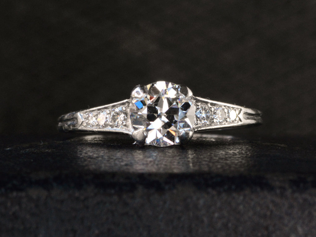 Front view of a c1930 Art Deco Tiffany & Co platinum engagement ring with a round old cut diamond and three smaller diamonds on each shoulder, shown on dark background