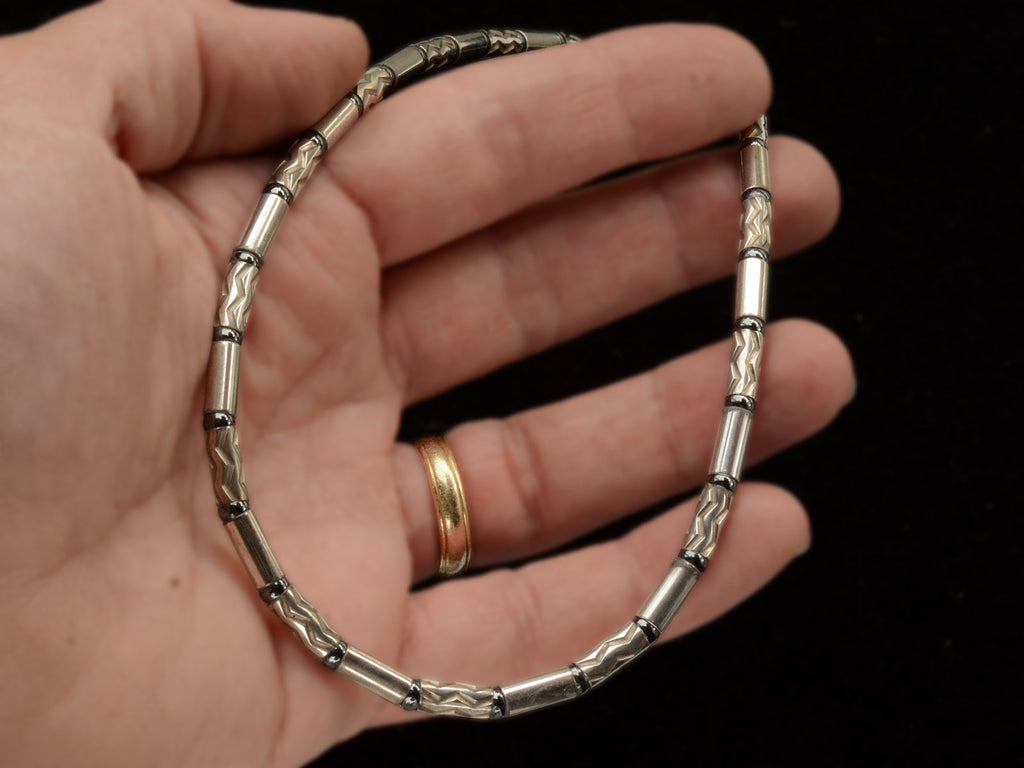 A vintage Tiffany "Aztec" necklace with barrel-shaped sterling silver beads interspersed with narrow bands of hematite and alternating with zig-zag embellished beads, shown held in hand.