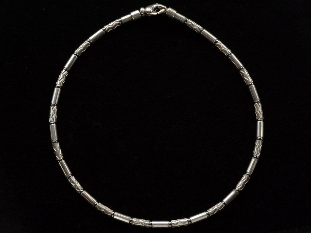 A vintage Tiffany "Aztec" necklace with barrel-shaped sterling silver beads interspersed with narrow bands of hematite and alternating with zig-zag embellished beads, shown on black background.
