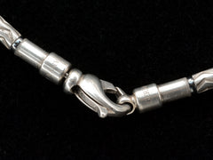 thumbnail of A close-up of a vintage Tiffany Aztec necklace with a lobster clasp and cylindrical links, shown against a black background. Stamps for "Tiffany & Co" and "Germany" are partially visible.
