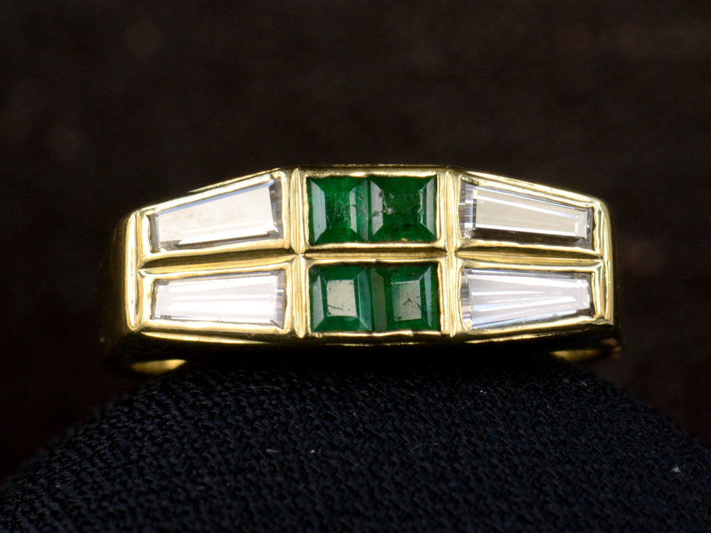 Front view of vintage yellow gold Tiffany ring with four square emeralds and four tapered diamond baguettes.  Shown on dark background.