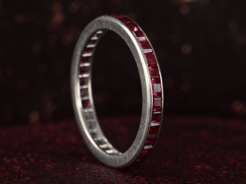 Angled view of c1950 Tiffany & Co platinum eternity band  with square cut rubies on dark textured background.