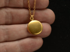 thumbnail of Small  gold round antique locket on chain, held in hand.