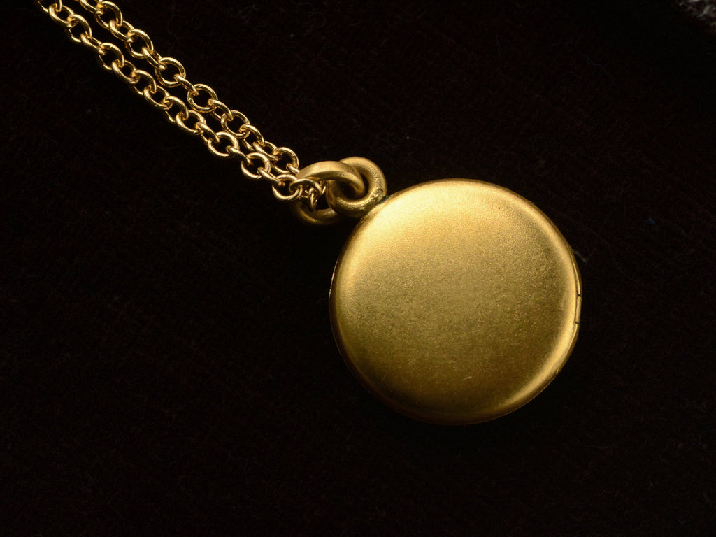 Small  gold round antique locket on chain, on black background.