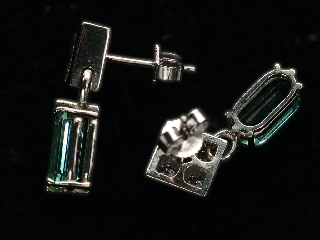 Alternate side profile and back view of c1990 white gold earrings with diamond-shaped diamond studded tops and teal tourmaline pendants (on black background).