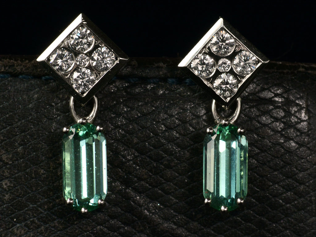 Front view of c1990 white gold earrings with diamond-shaped diamond studded tops and teal tourmaline pendants (on dark background). 