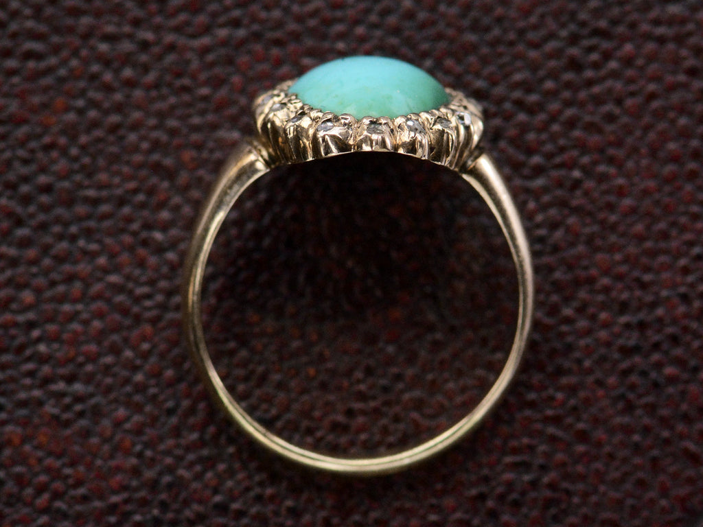Side profile of antique rose gold ring with egg shaped turquoise surrounded by small rose cut diamonds, shown on dark textured background.