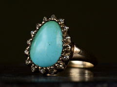 thumbnail of Angled view of antique rose gold ring with egg shaped turquoise surrounded by small rose cut diamonds, shown on dark background.