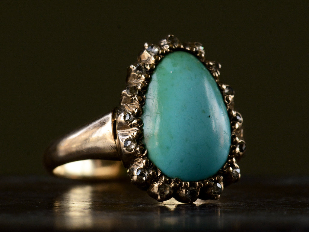 Left angled view of antique rose gold ring with egg shaped turquoise surrounded by small rose cut diamonds, shown on dark background.