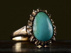 thumbnail of Left angled view of antique rose gold ring with egg shaped turquoise surrounded by small rose cut diamonds, shown on dark background.