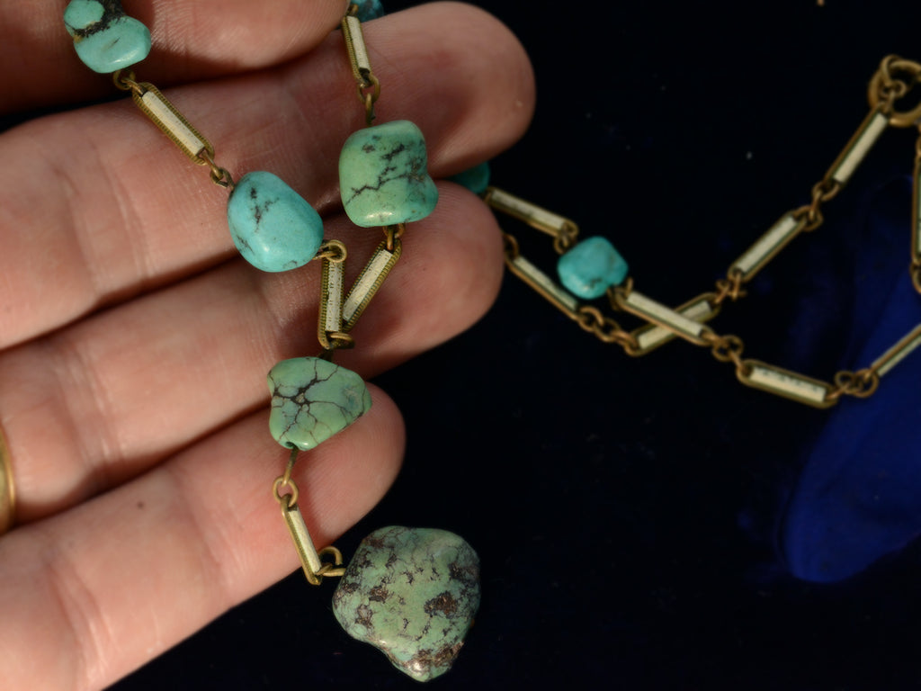 Detail view of c1920 Art Deco turquoise nugget and white enamel brass chain necklace, shown on hand for scale