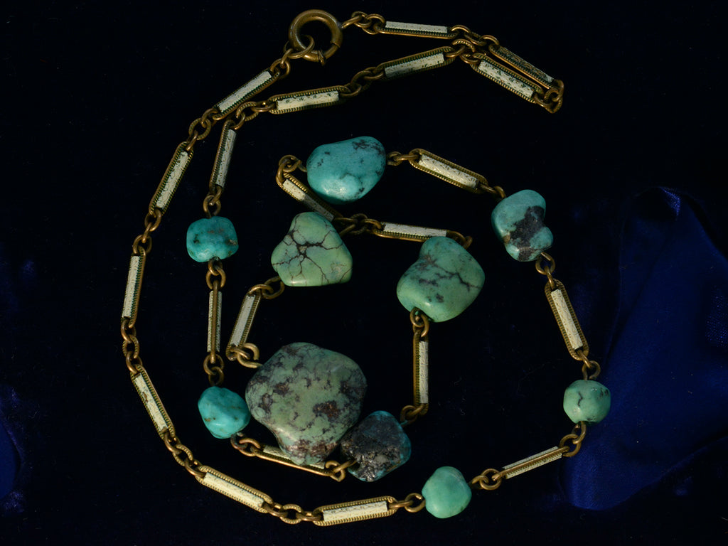 Close up view of c1920 Art Deco turquoise nugget and white enamel brass chain necklace, shown on dark blue background