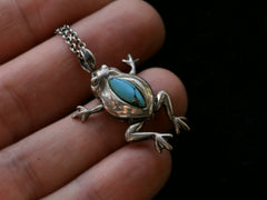 thumbnail of Silver frog pendant with turquoise stone held between fingers against a dark background