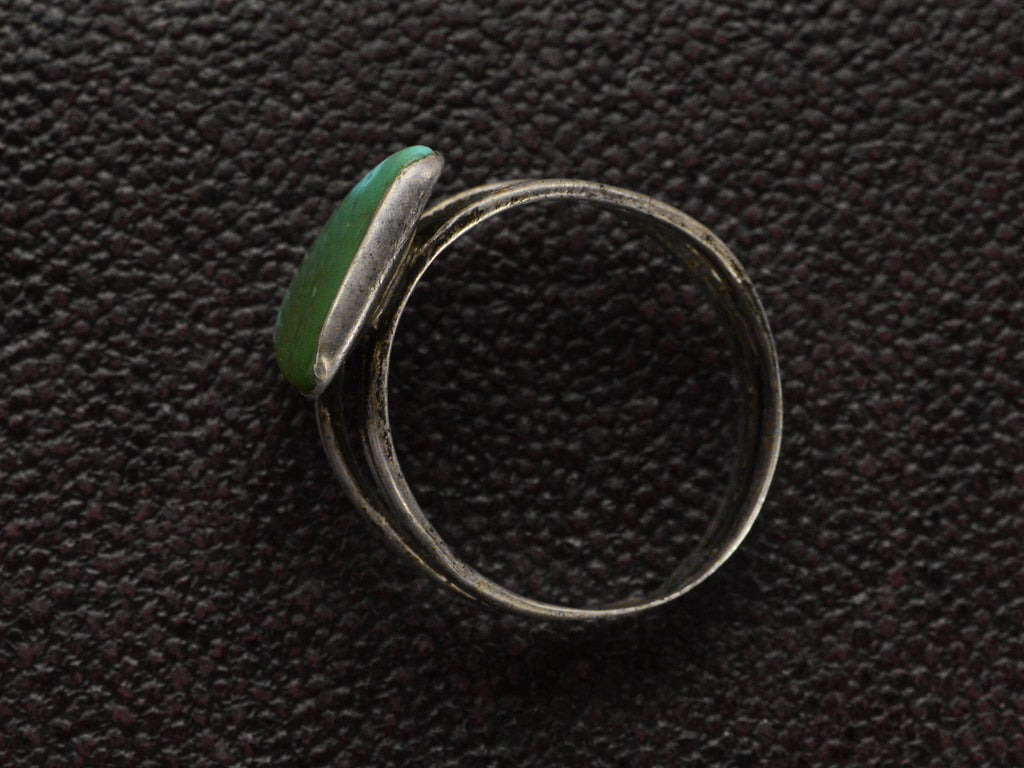 Side profile view of a sterling silver ring featuring a large, polished green triangular turquoise stone with natural matrix lines, set against a dark textured background.