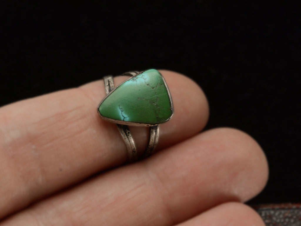 A sterling silver ring featuring a large, polished green triangular turquoise stone with natural matrix lines, shown worn on finger