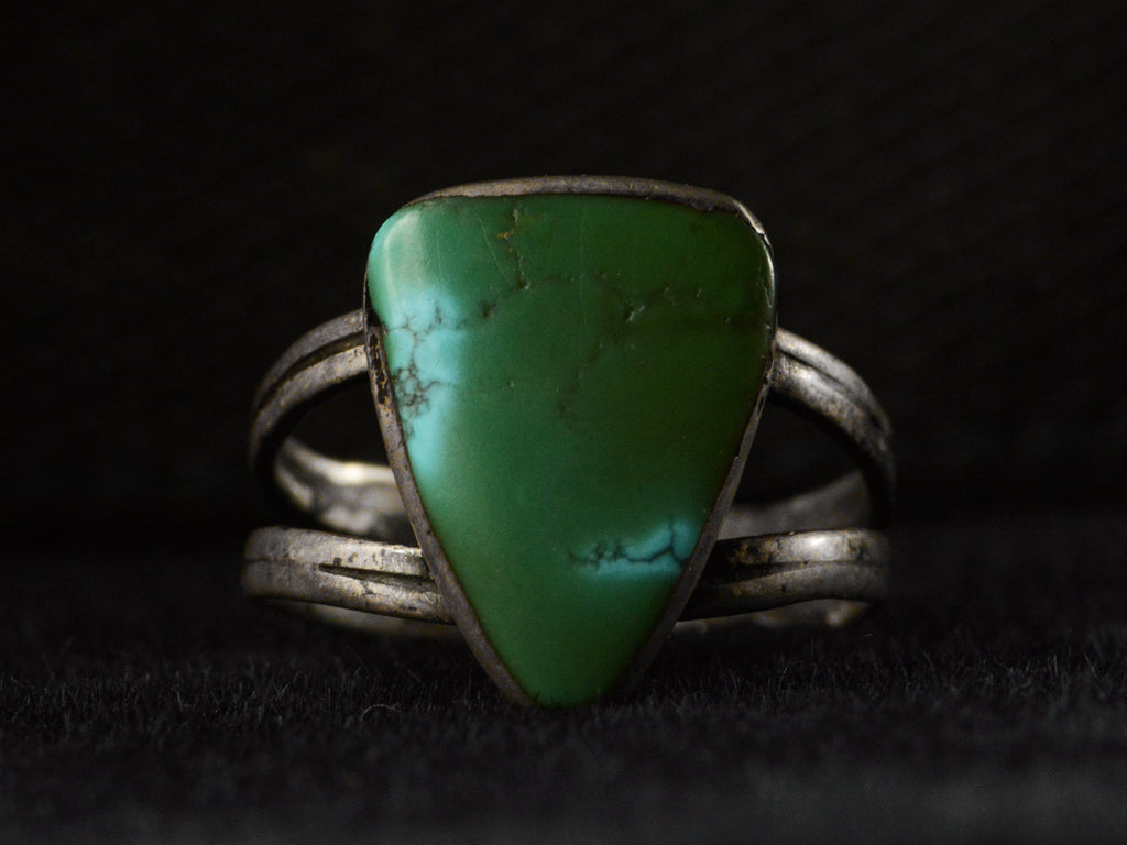 Front view of a sterling silver ring featuring a large, polished green triangular turquoise stone with natural matrix lines, set against a dark background.
