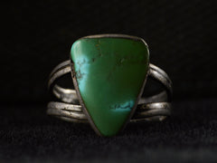 thumbnail of Front view of a sterling silver ring featuring a large, polished green triangular turquoise stone with natural matrix lines, set against a dark background.